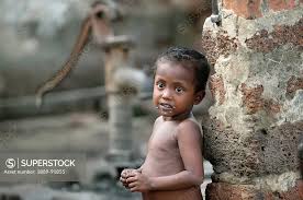 A naked child standing against a wall with a water hand pump in ...