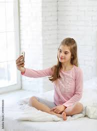 charming girl 8-10 years old on a white bed with a phone on the ...